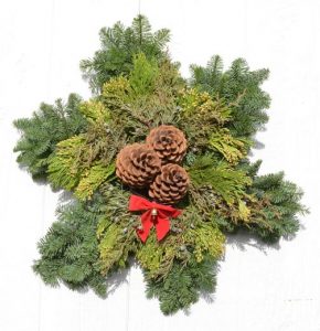 snowflake shaped wreath with yellow cedar, blue juniper berries and three pinecones in the middle